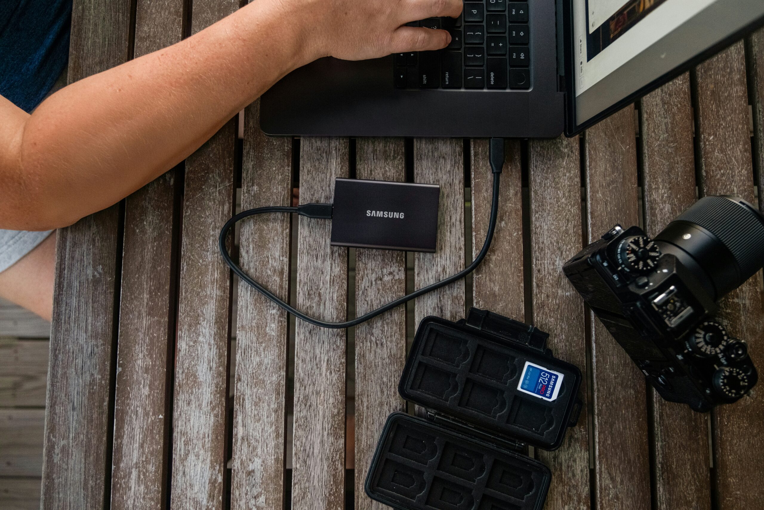 Person checking whether photos are backed up using a laptop, external SSD, camera, and memory card.